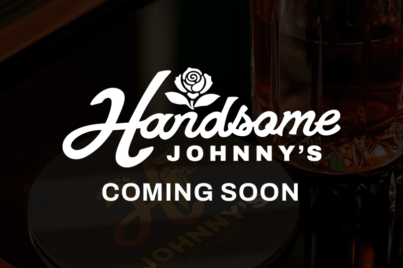 Handsome Johnny's Main logo in white overlaid a dark photograph of a branded coaster and bartop